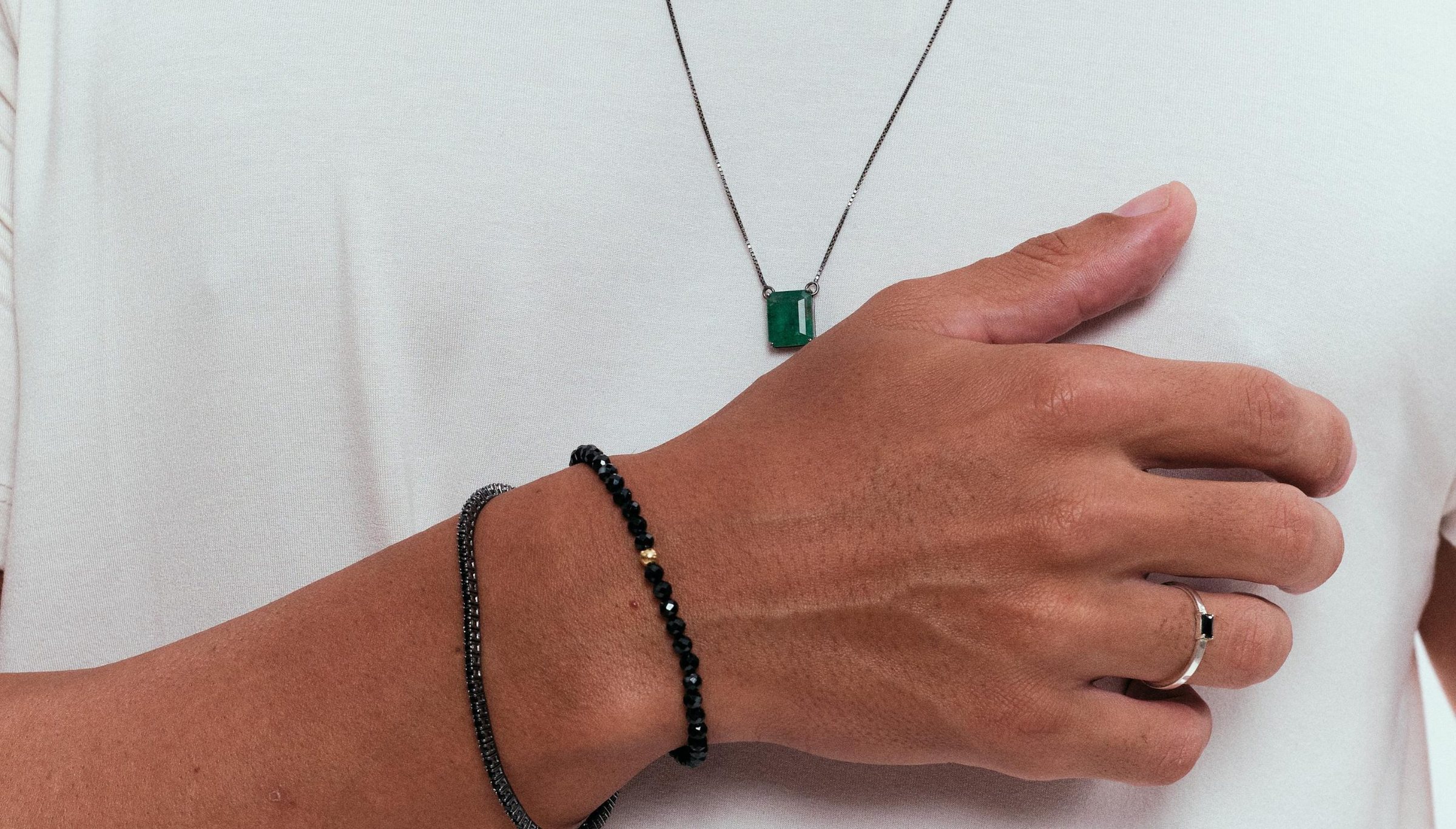 Pingente de esmeralda e pulseiras, sobre camiseta branca